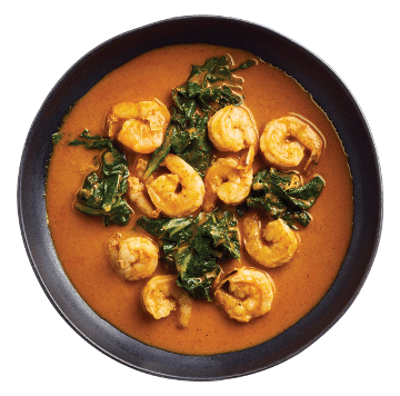 Shrimp curry with wilted greens served in a dark bowl, in a rich orange sauce.
