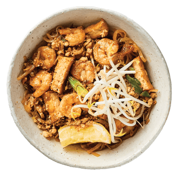 Bowl of stir-fried noodles with shrimp, tofu, bean sprouts, and green onions in a light brown sauce.